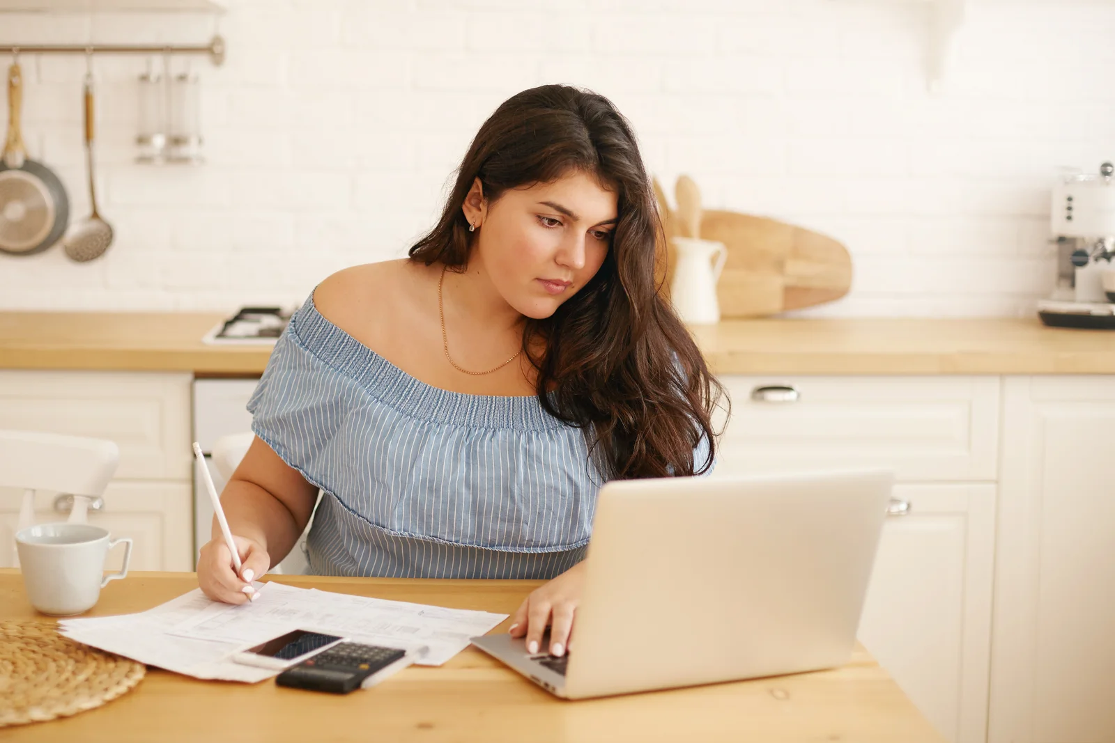 Woman taking notes beside her laptop while planning a budget at home
