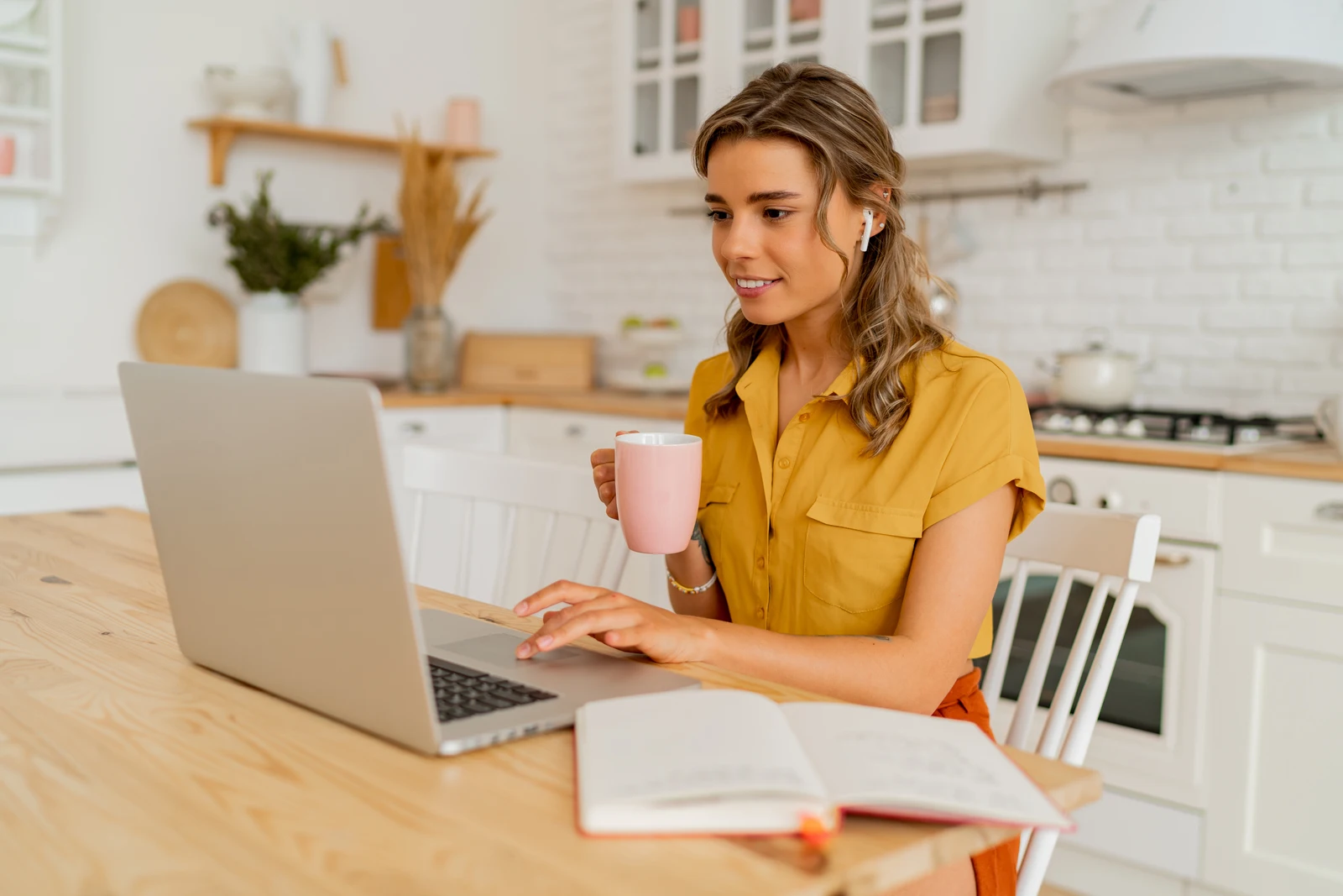 Smiling woman working on a laptop in her kitchen during breakfast